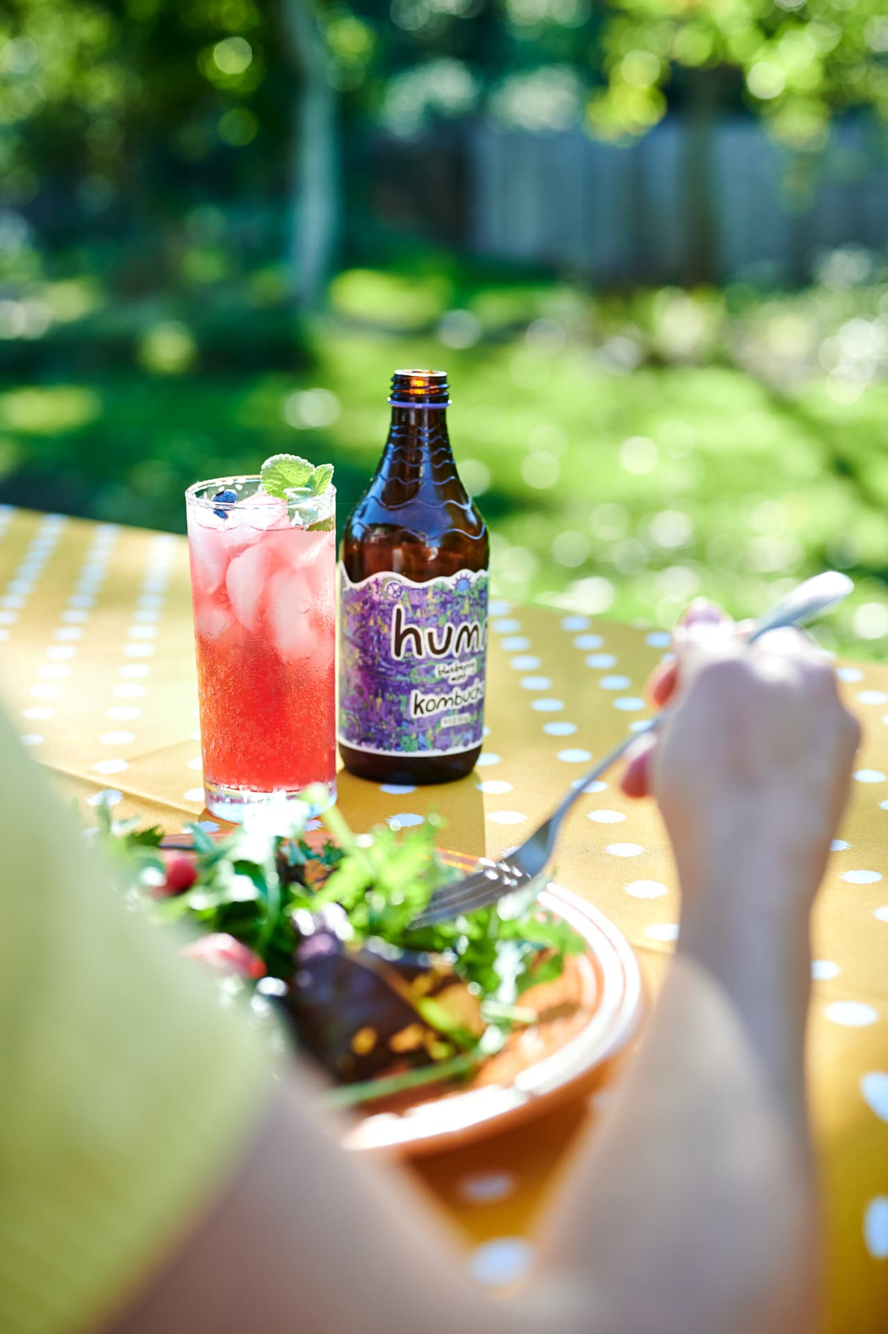 Humm blackberry mint kombucha cocktail on a sunny garden table with a salad