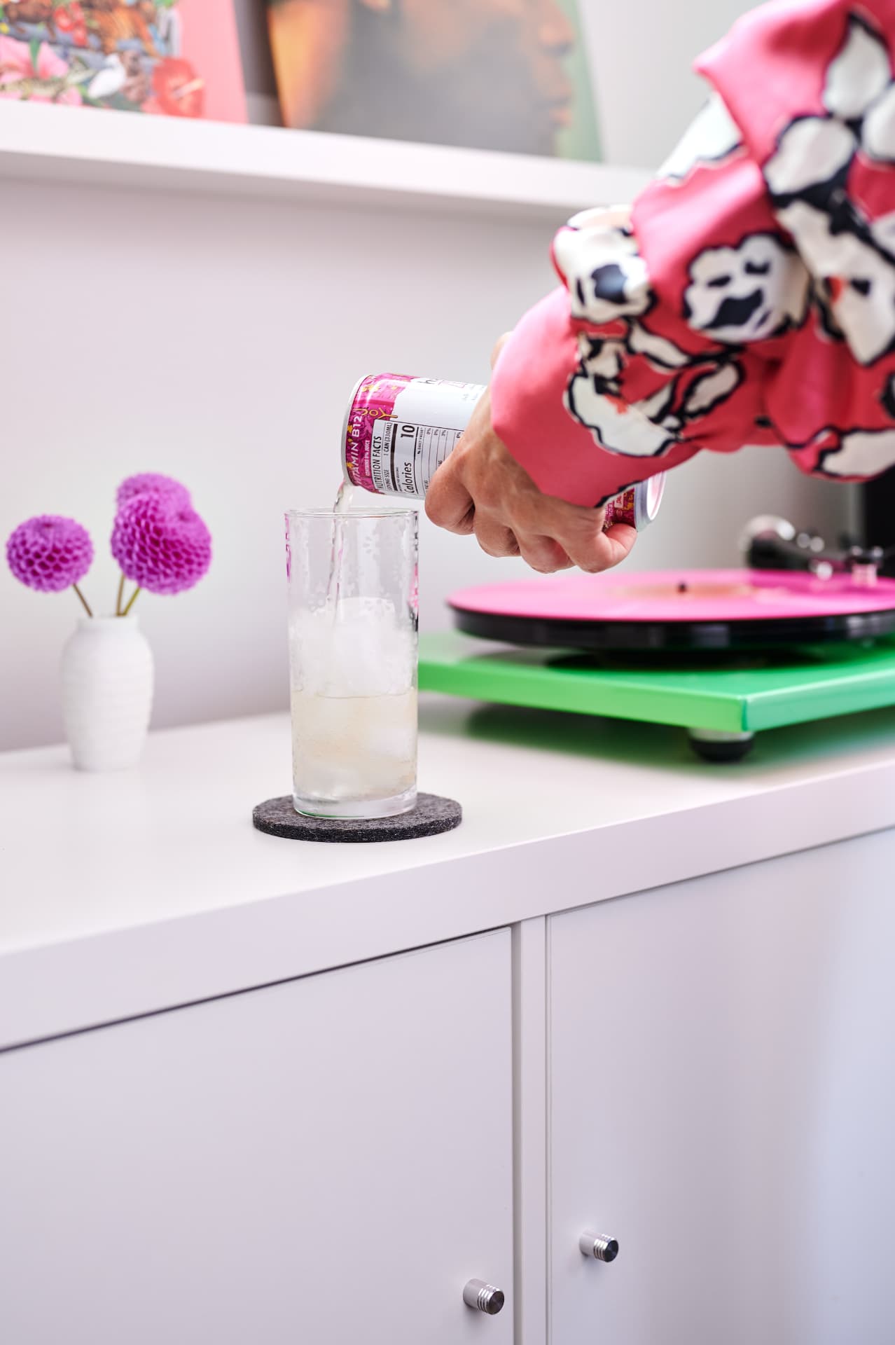 Pouring Humm kombucha into a glass beside a record player