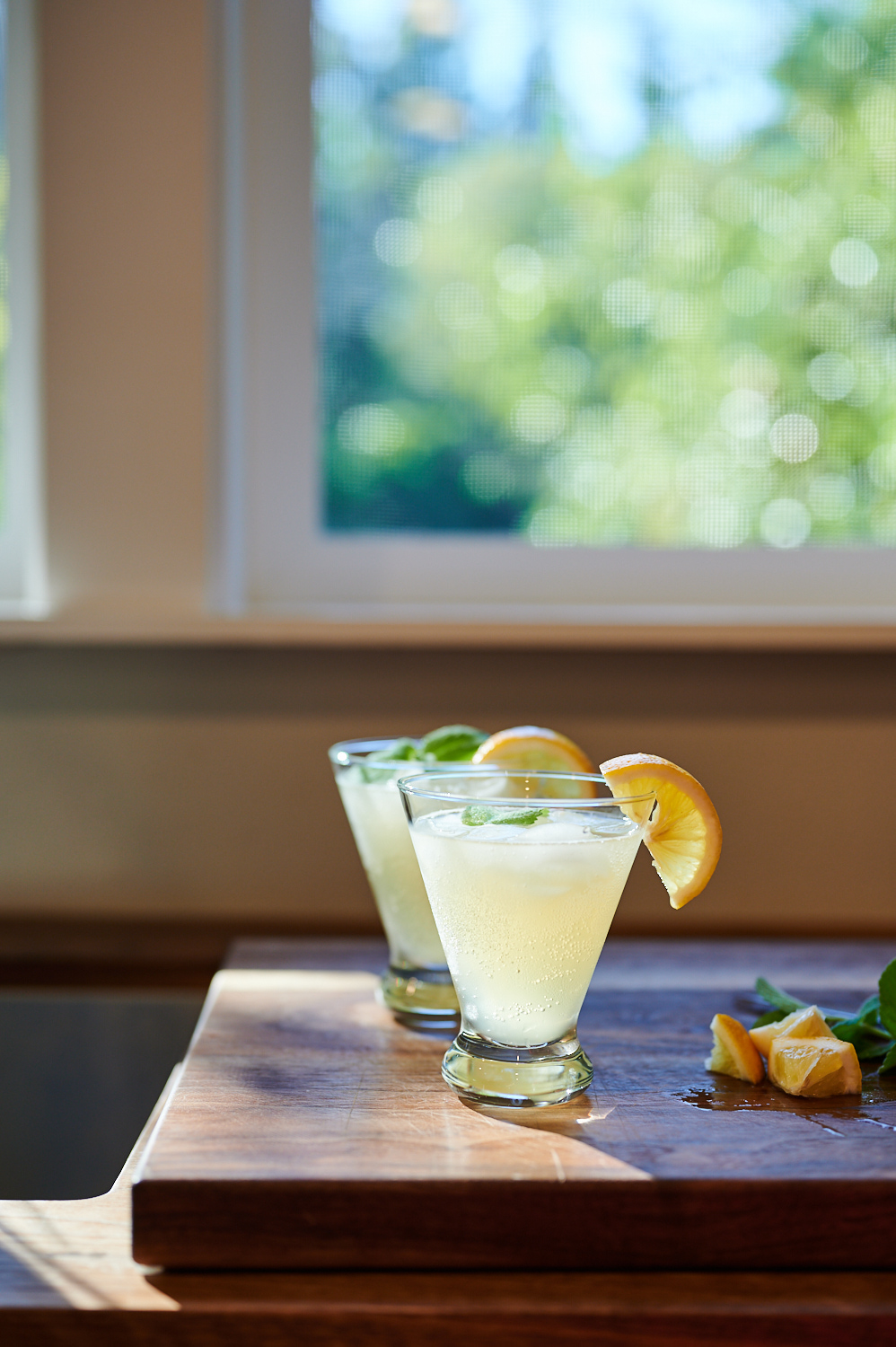 Two lemon-garnished kombucha cocktails on a wood board by a window